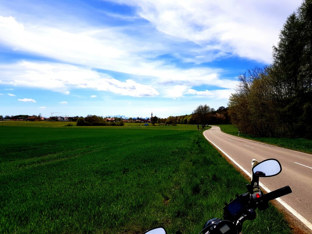Asphalt in Kurven geschwungen, sattes Grün und die Berge im Blick.